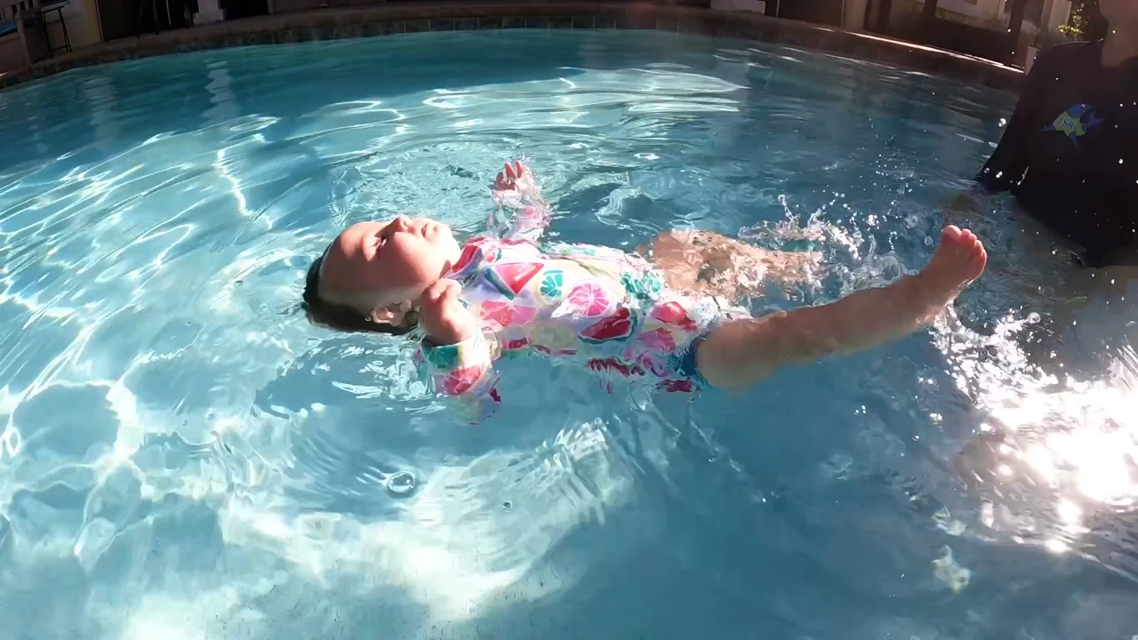 A young child floating on their back in a swimming pool