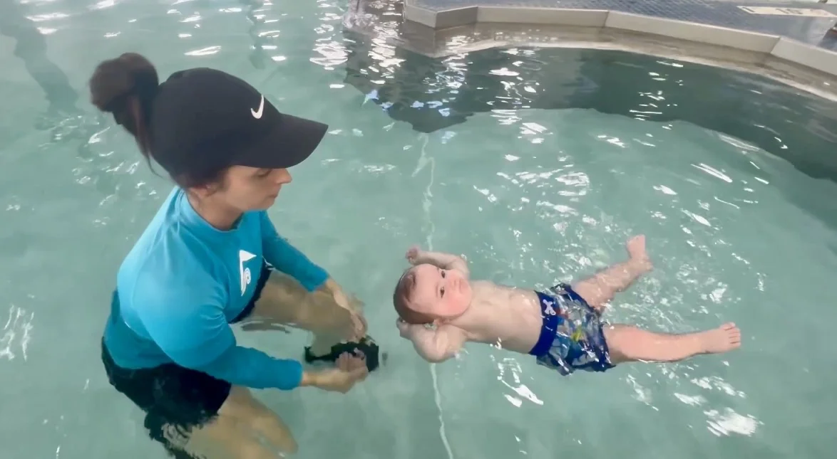 An instructor beside a child practicing a back float in a swimming pool